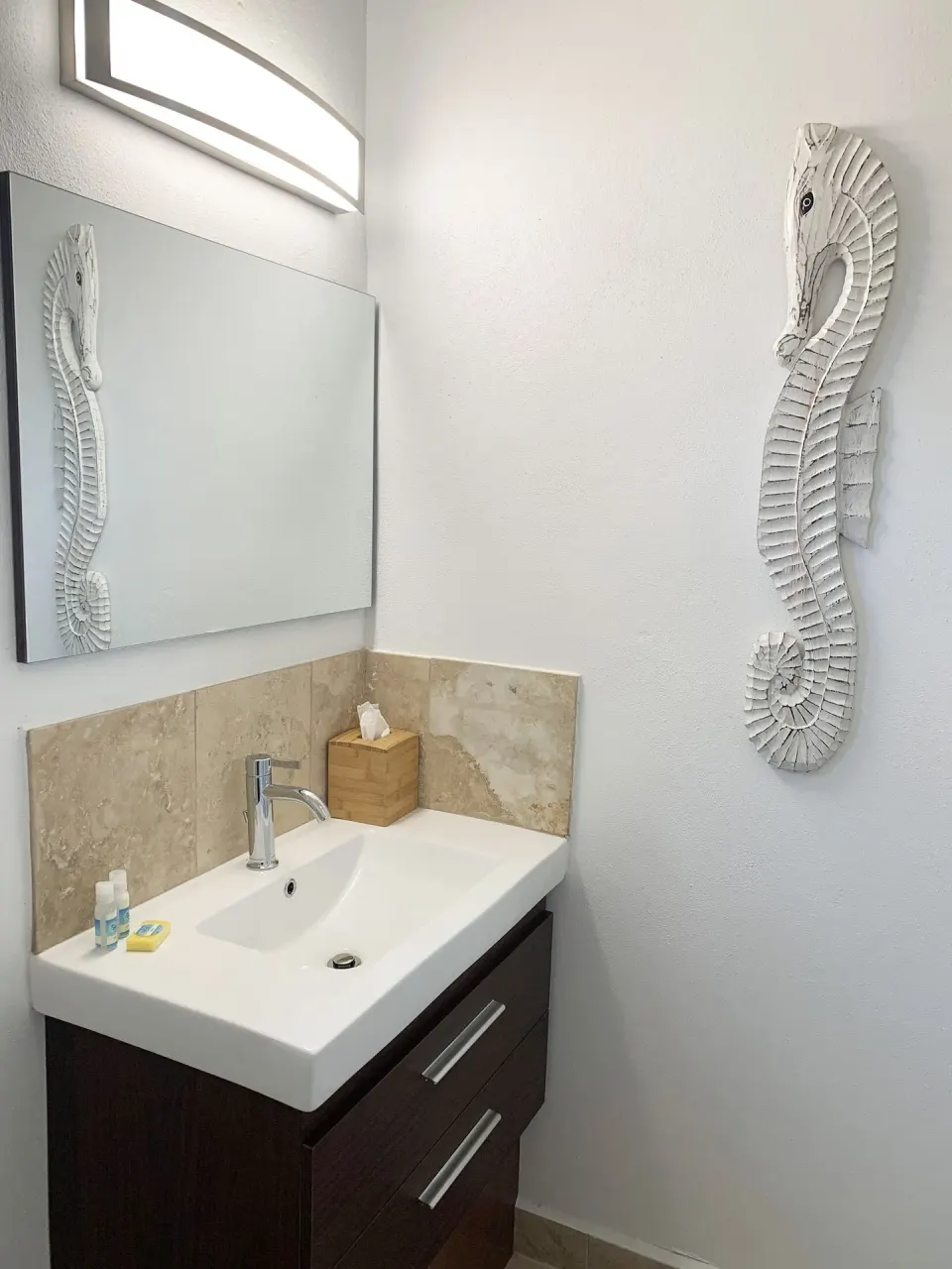 Studio bathroom vanity at Sand Castle on the Beach with mirror, sink, amenities, and seahorse wall art.