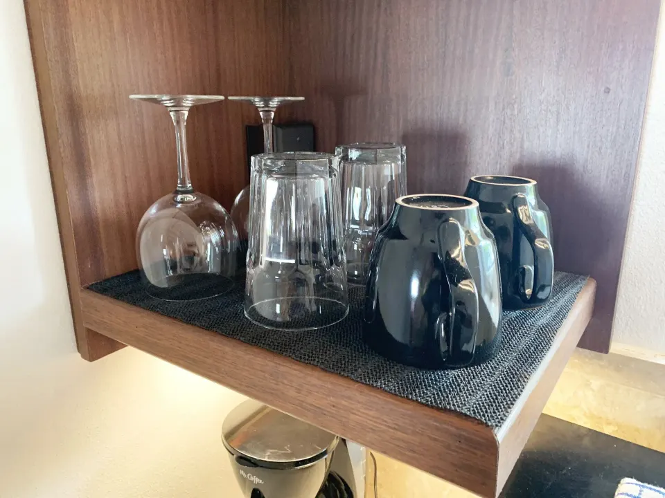 Studio shelf with wine glasses, tumblers, and dark mugs at Sand Castle on the Beach.