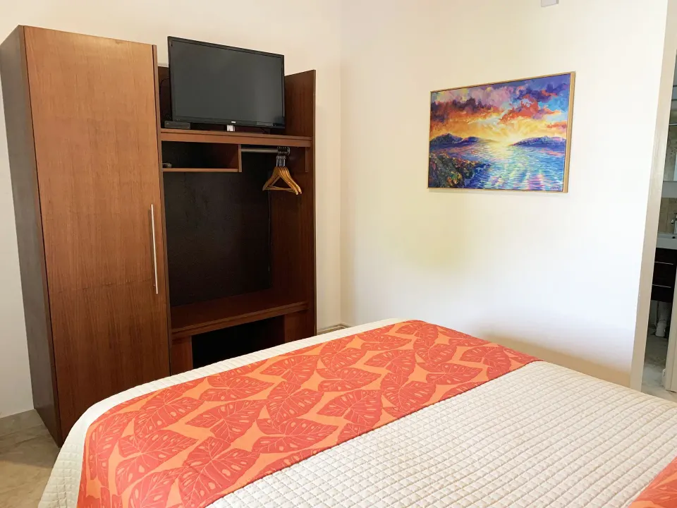Studio bed facing a wood wardrobe with TV and open closet at Sand Castle on the Beach.
