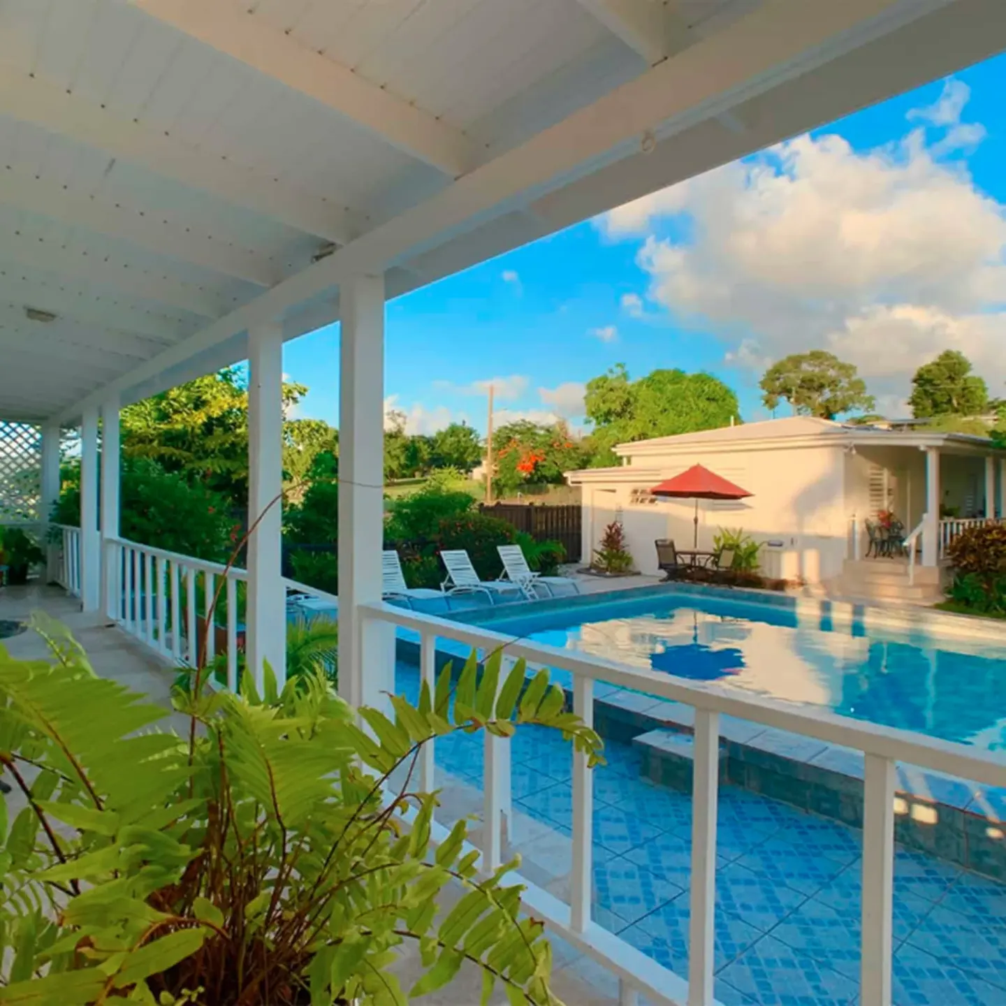 Studio porch overlooking the pool at Sand Castle on the Beach, with lounge chairs and tropical plants.