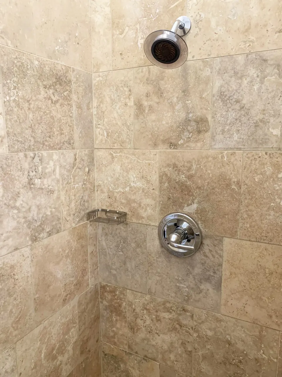 Studio shower at Sand Castle on the Beach with stone-look tile, chrome fixtures, and a corner soap dish.