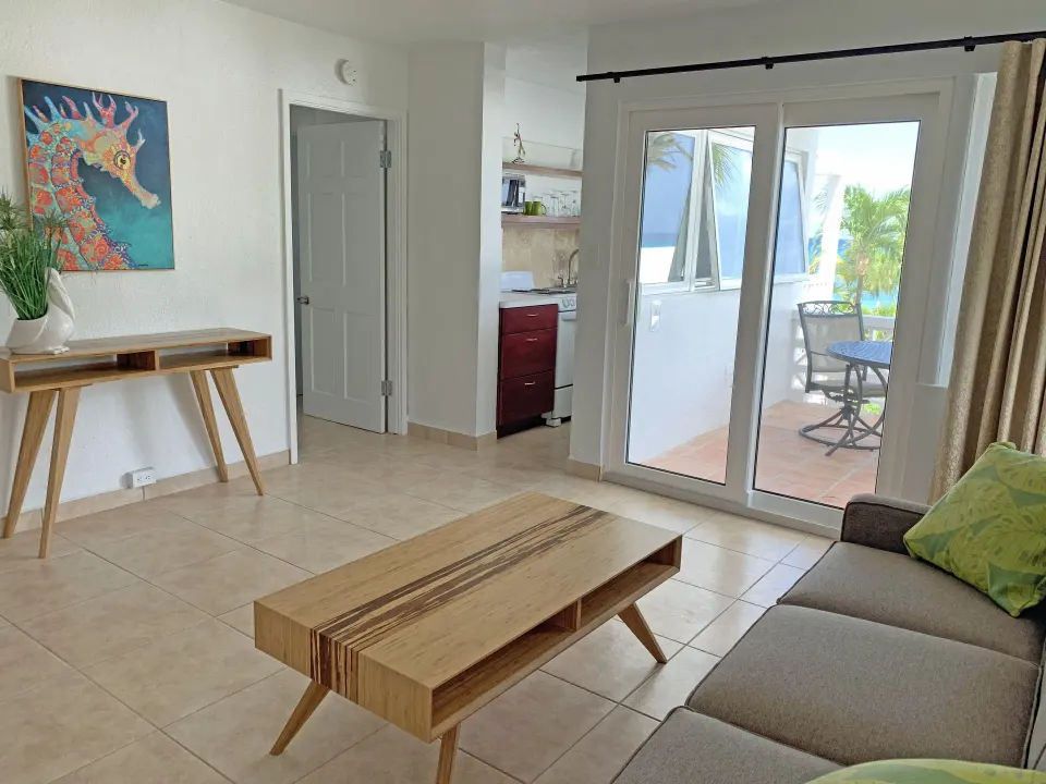 Suite living room with sofa bed, coffee table, kitchenette, and balcony doors at Sand Castle on the Beach.