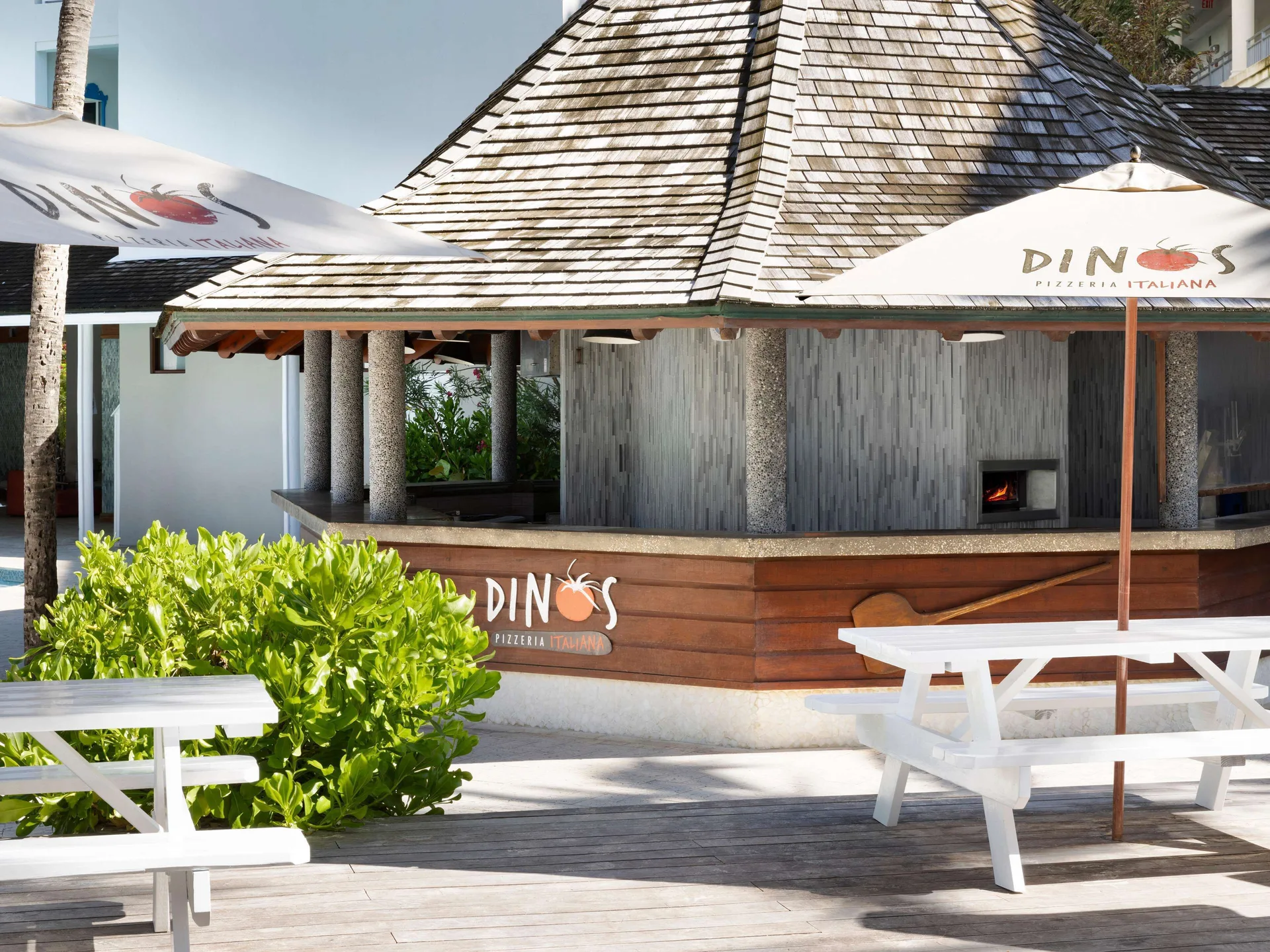 Dino's Pizzeria exterior with umbrellas, picnic tables and a visible oven at Sandals Barbados.