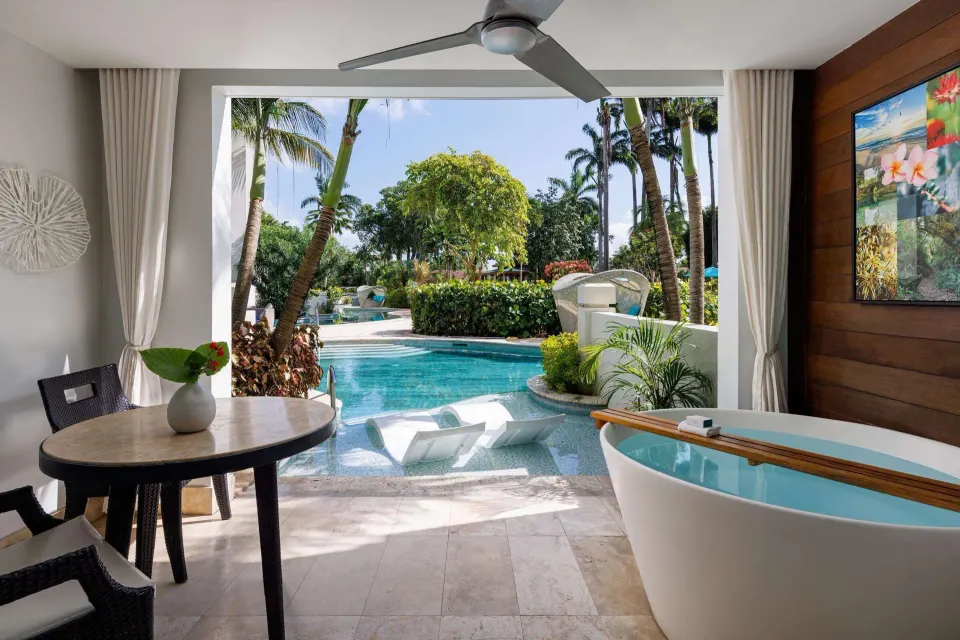 Covered patio with soaking tub beside a lagoon pool and gardens at Sandals Barbados.