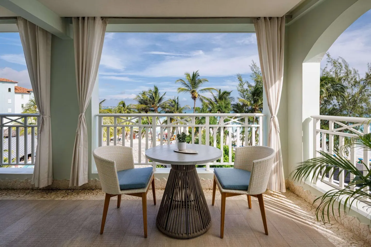 Covered balcony with table, two chairs, palms, and ocean view at Sandals Barbados.