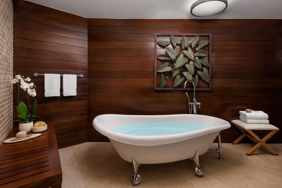 Bathroom soaking tub with wood walls, towels, and leaf artwork at Sandals Barbados.
