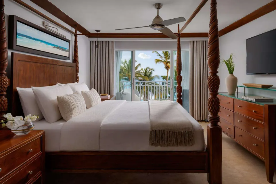 Four-poster king bed, dresser, TV, and ocean-facing balcony at Sandals Barbados.