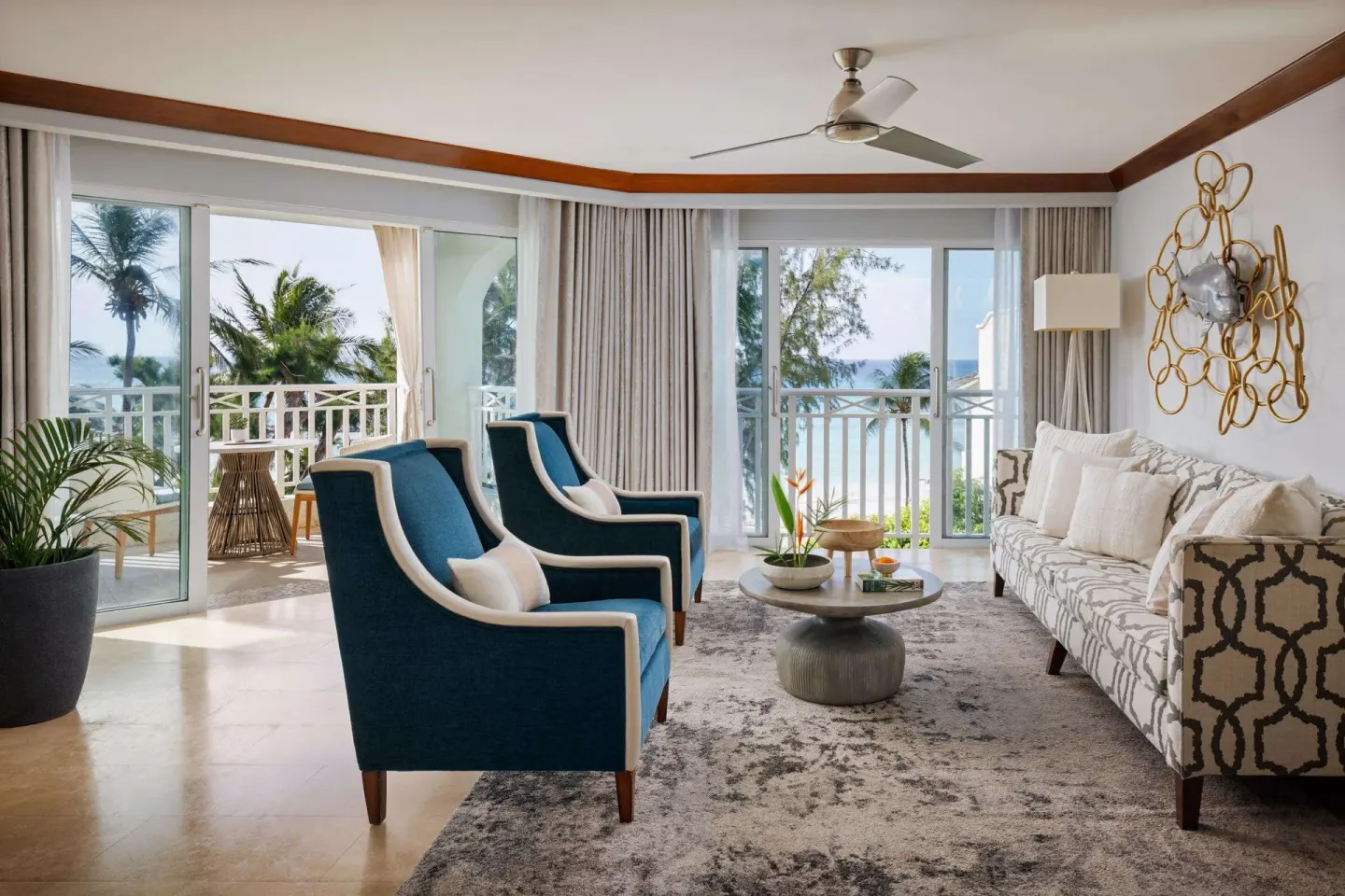 Living area with blue armchairs, patterned sofa, coffee table, and ocean view at Sandals Barbados.