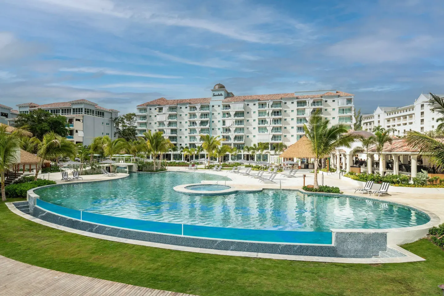 Large curved resort pool with balconies and palms at Sandals Dunns River.
