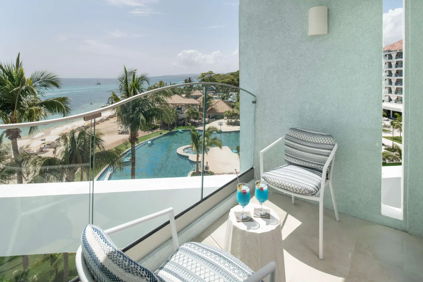 Balcony with chairs, drinks, beach, and pool view at Sandals Dunns River.