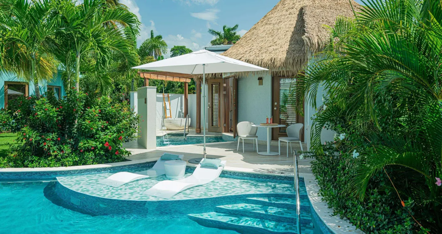 Poolside villa patio with thatched roof and in-water loungers at Sandals Dunns River.