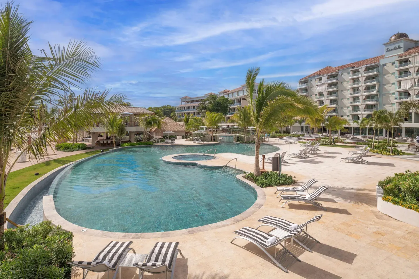 Sunlit pool deck with striped loungers and palm trees at Sandals Dunns River.