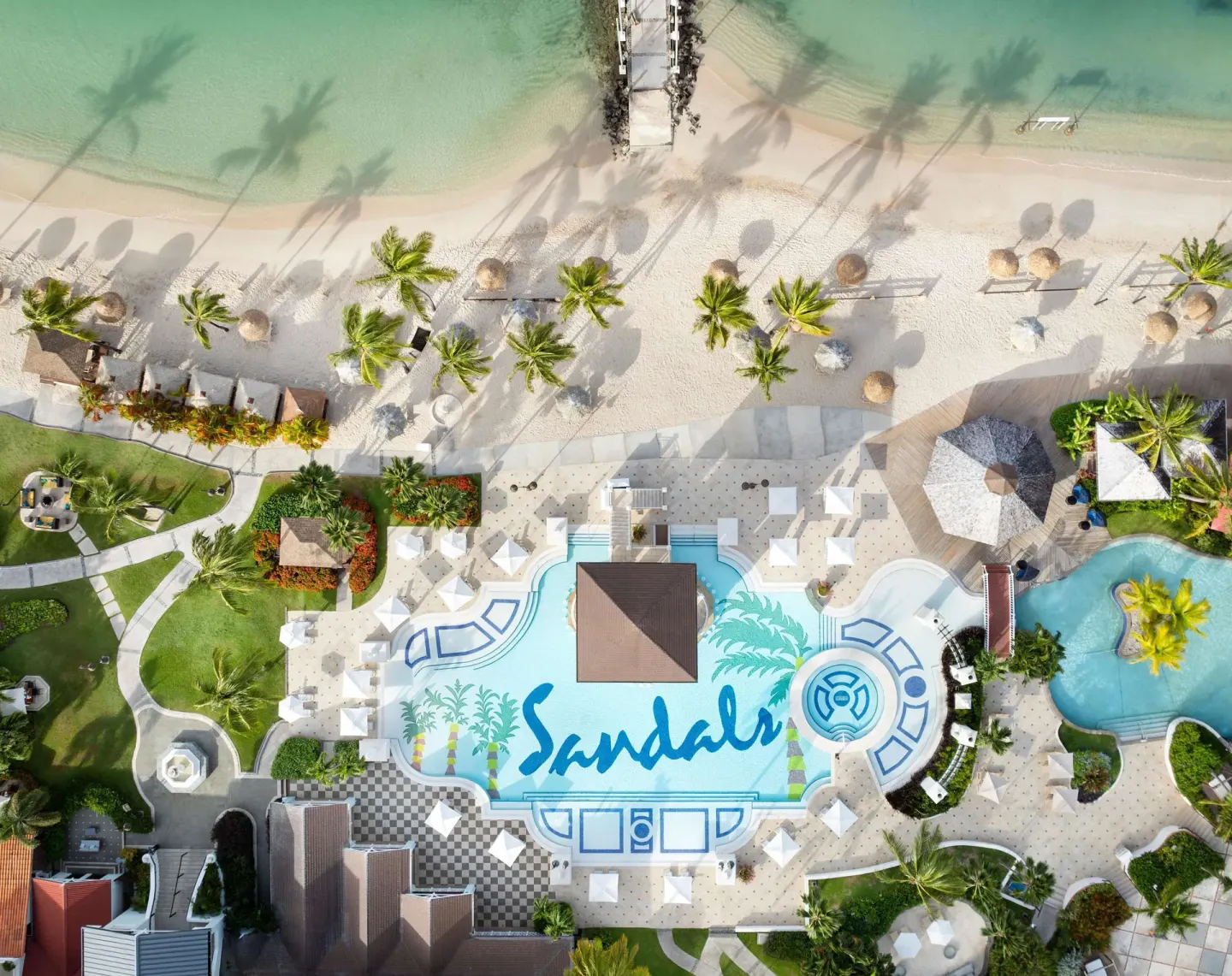 Aerial view of the pool, beach, palms, and pier at Sandals Grande St. Lucian.
