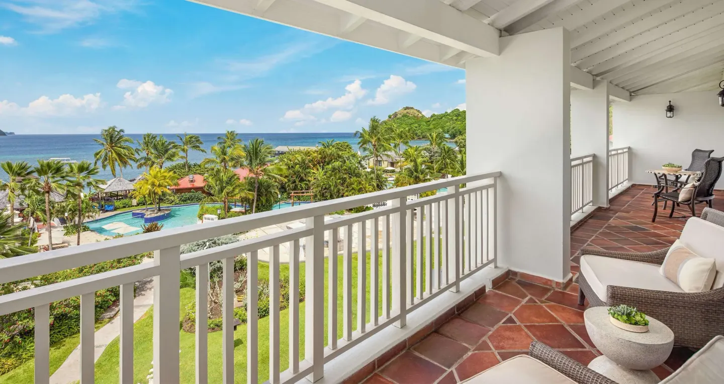 Balcony with wicker seating overlooking pools and ocean at Sandals Grande St. Lucian.