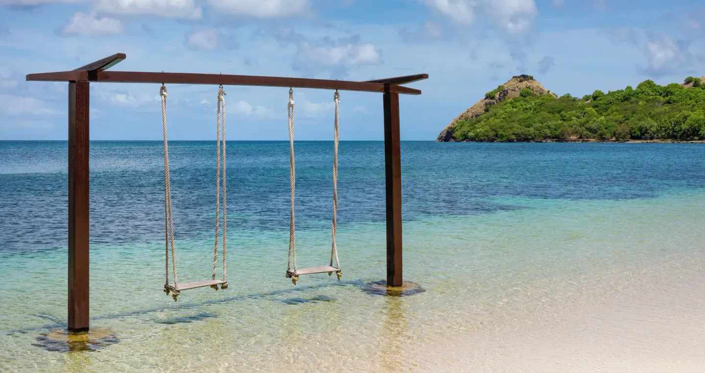Overwater swings at Sandals Grande St. Lucian set in shallow clear water near a green headland.