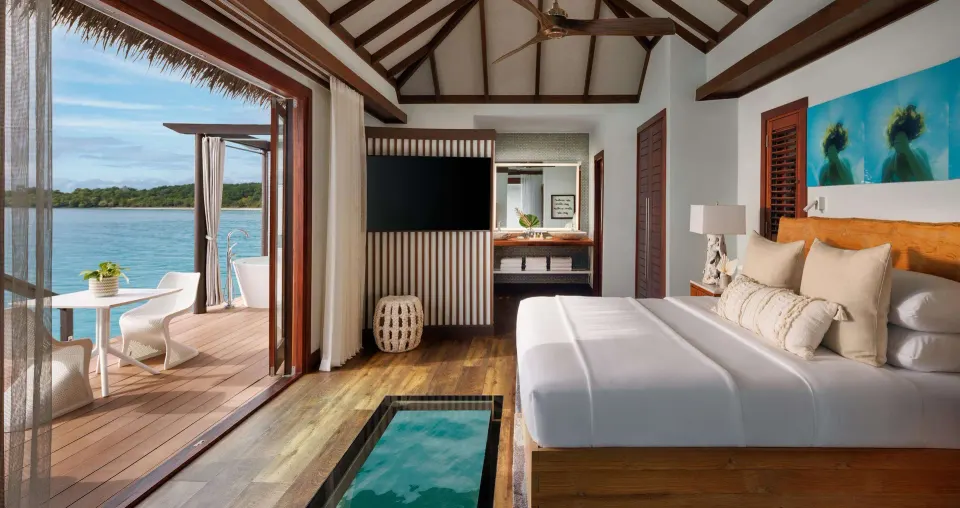 Overwater guest room with a king bed, glass floor panel, and deck at Sandals Grande St. Lucian.