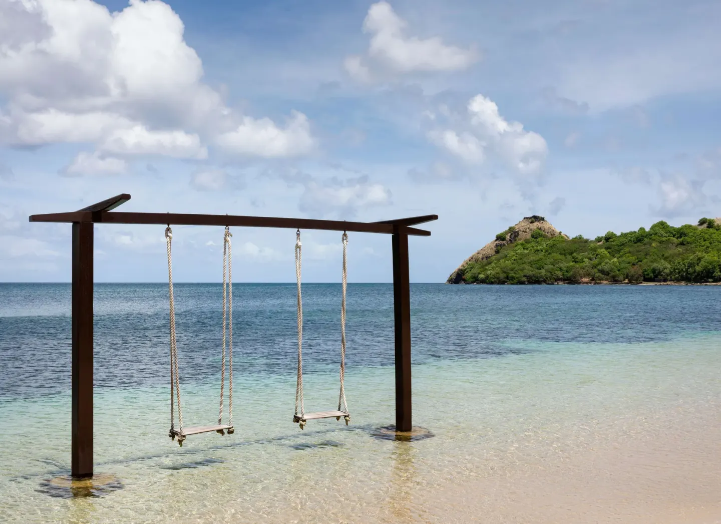 Two overwater swings at Sandals Grande St. Lucian with a blue bay and green hillside beyond.