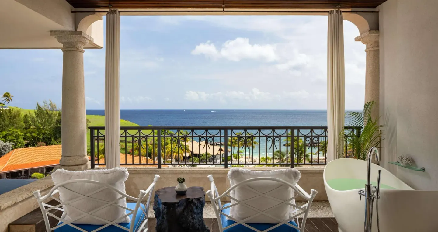 Covered balcony with chairs, soaking tub, and ocean view at Sandals Grenada.