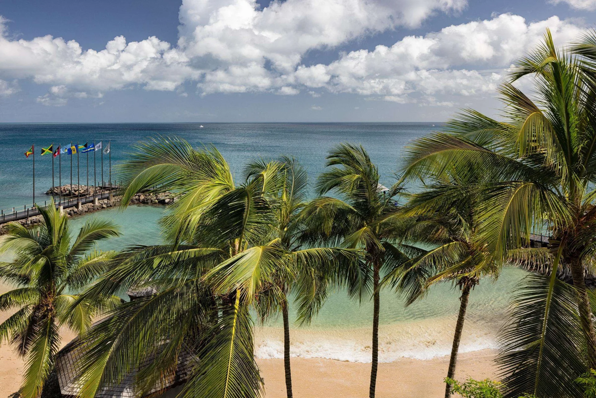 Palm trees frame the beach, turquoise sea, and flag-lined jetty at Sandals Grenada.