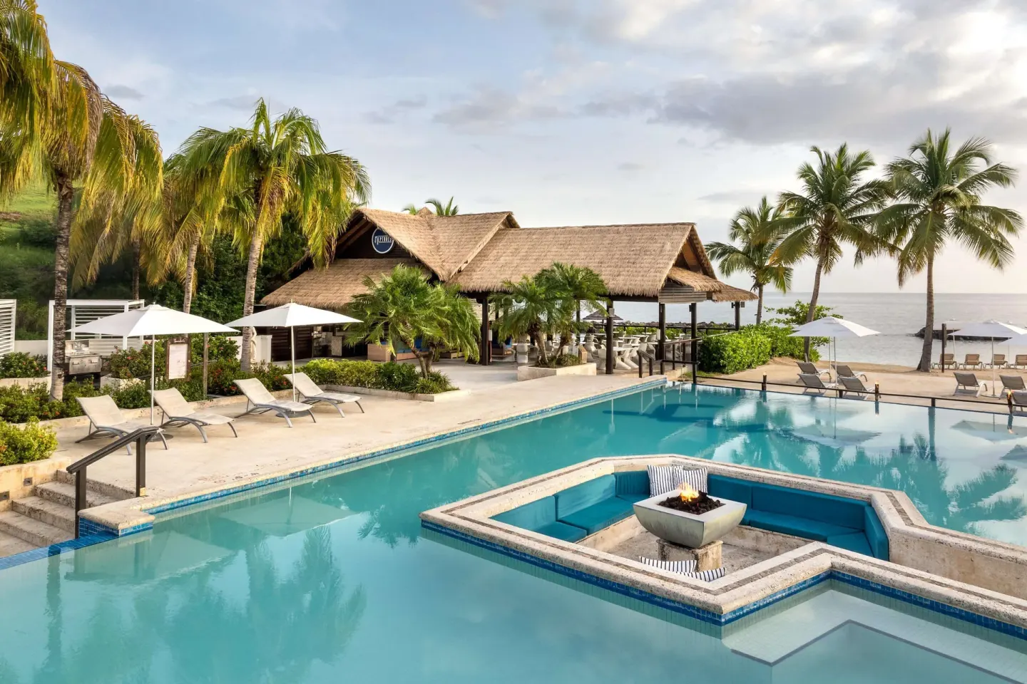 Beachfront pool with in-water fire pit, loungers, palms, and ocean at Sandals Grenada.