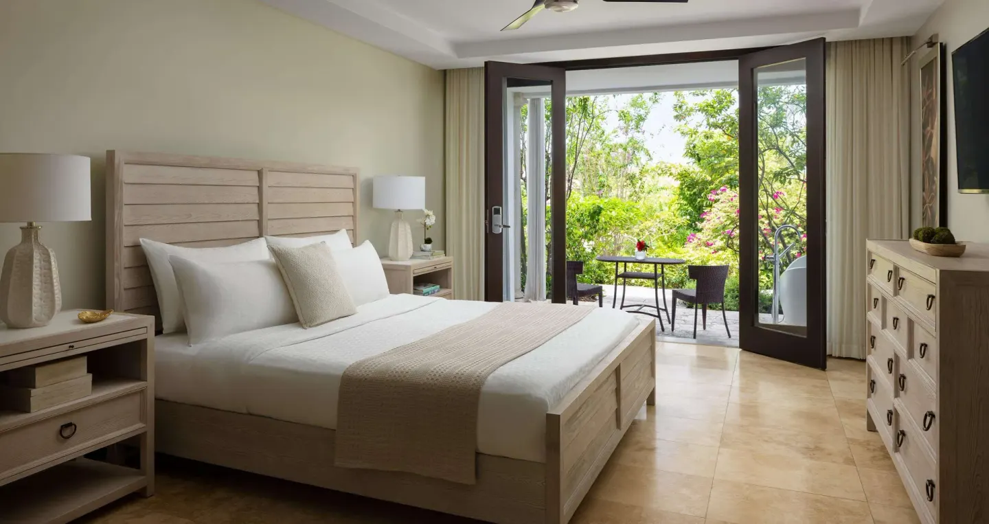 Guest room with a king bed, dresser, and garden patio at Sandals Grenada.