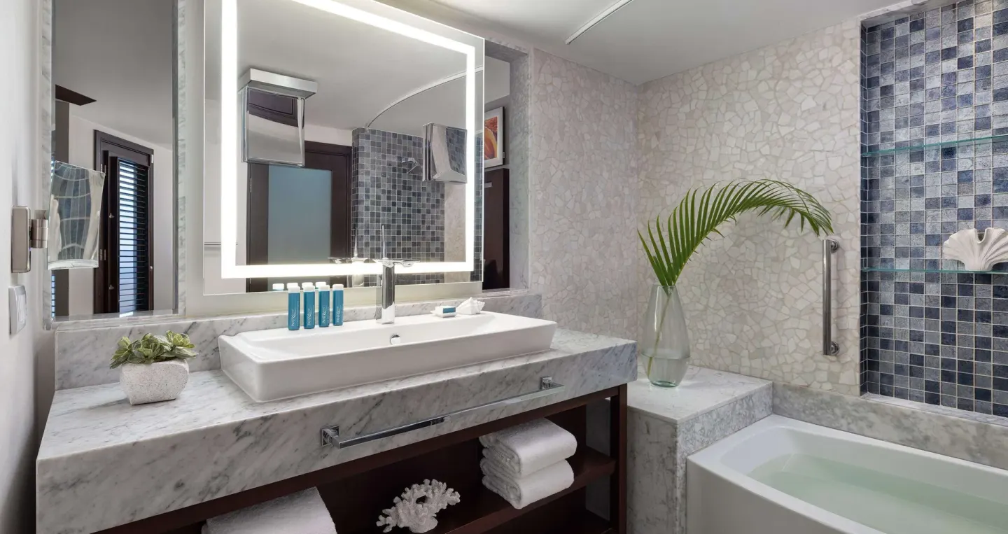 Guest bathroom with marble vanity, lit mirror and bathtub at Sandals Grenada.