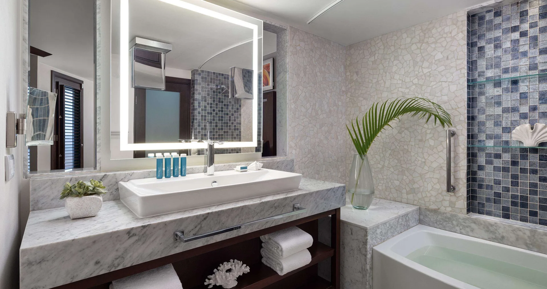 Guest bathroom with marble vanity, lit mirror and bathtub at Sandals Grenada.