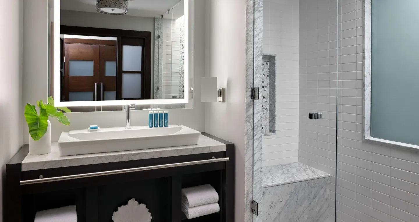 Guest bathroom with vanity, lit mirror and glass shower at Sandals Grenada.