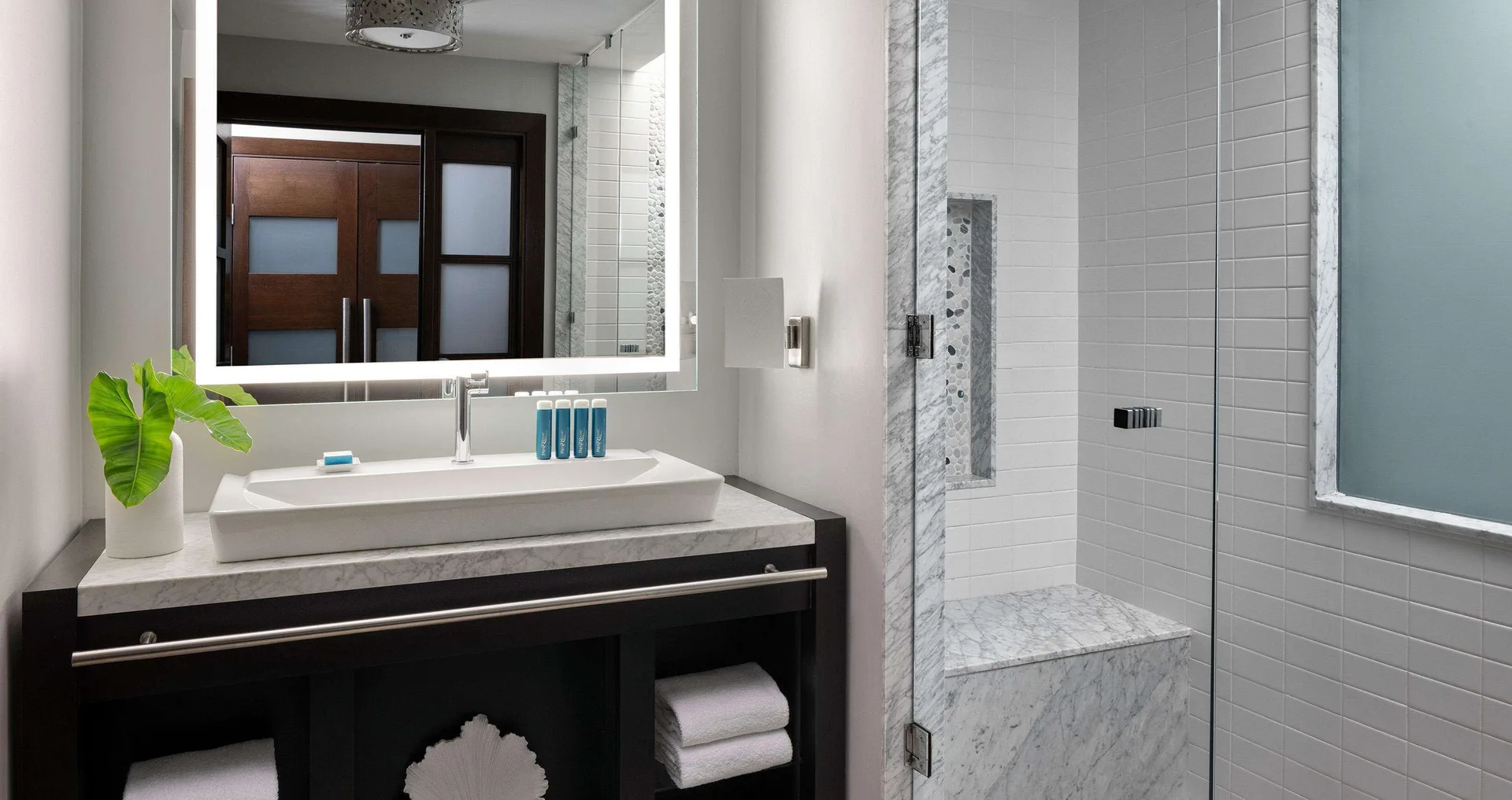 Guest bathroom with vanity, lit mirror and glass shower at Sandals Grenada.
