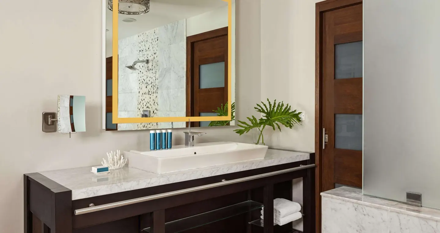 Guest bathroom vanity with gold-framed mirror and frosted glass shower at Sandals Grenada.