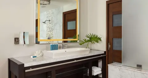 Guest bathroom vanity with gold-framed mirror and frosted glass shower at Sandals Grenada.