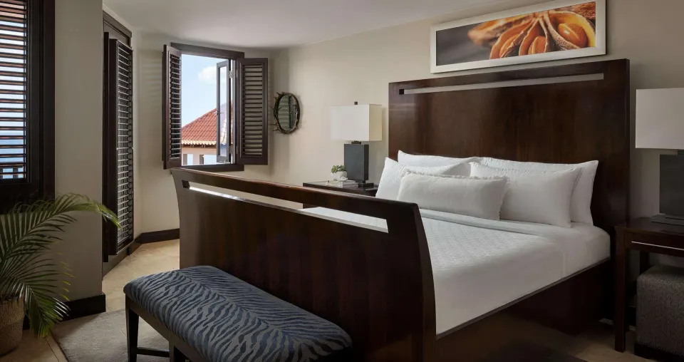 Guest room with a dark wood king bed, bench, and shuttered windows at Sandals Grenada.