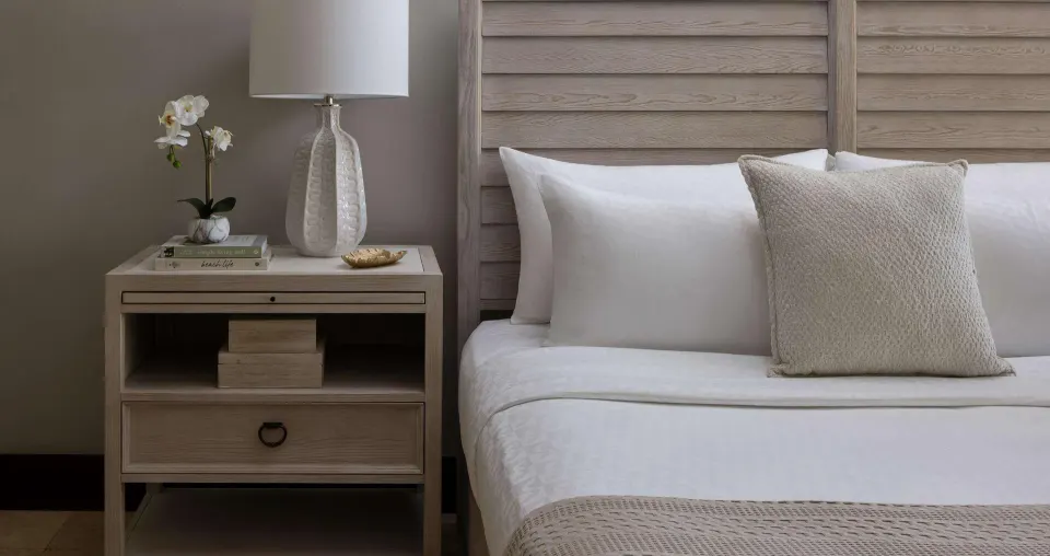 Close-up of a king bed, nightstand, lamp, and orchid at Sandals Grenada.