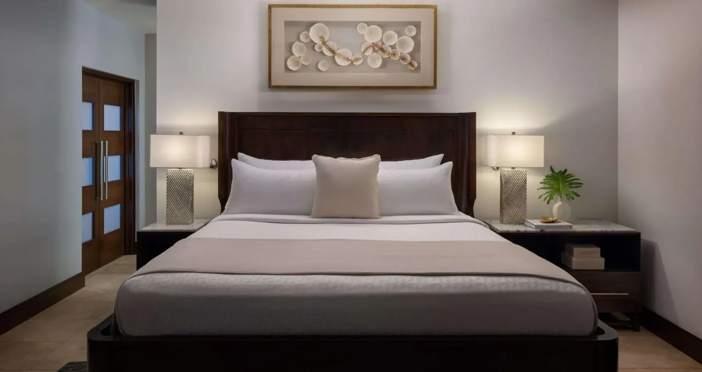 King bed with white linens and bedside lamps in a guest room at Sandals Grenada.