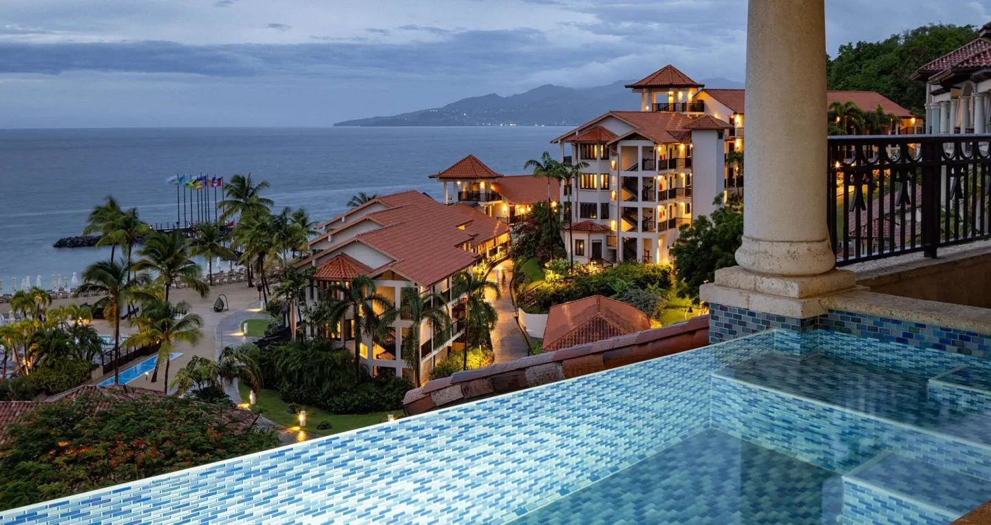 Evening view of an infinity pool, resort buildings, and coastline at Sandals Grenada.