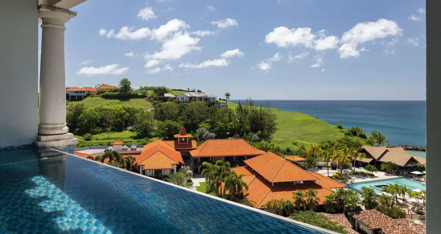 Infinity pool with hillside, orange rooftops, and ocean view at Sandals Grenada.