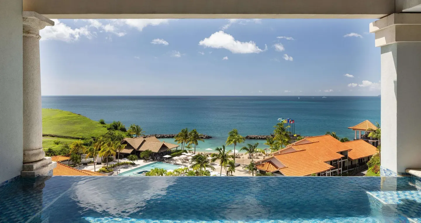 Infinity pool edge overlooking the beach, ocean, and resort rooftops at Sandals Grenada.