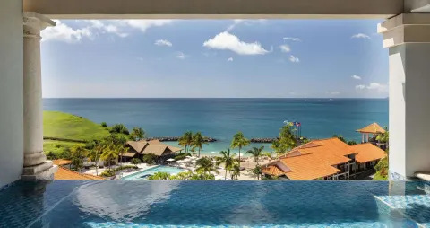Infinity pool edge overlooking the beach, ocean, and resort rooftops at Sandals Grenada.