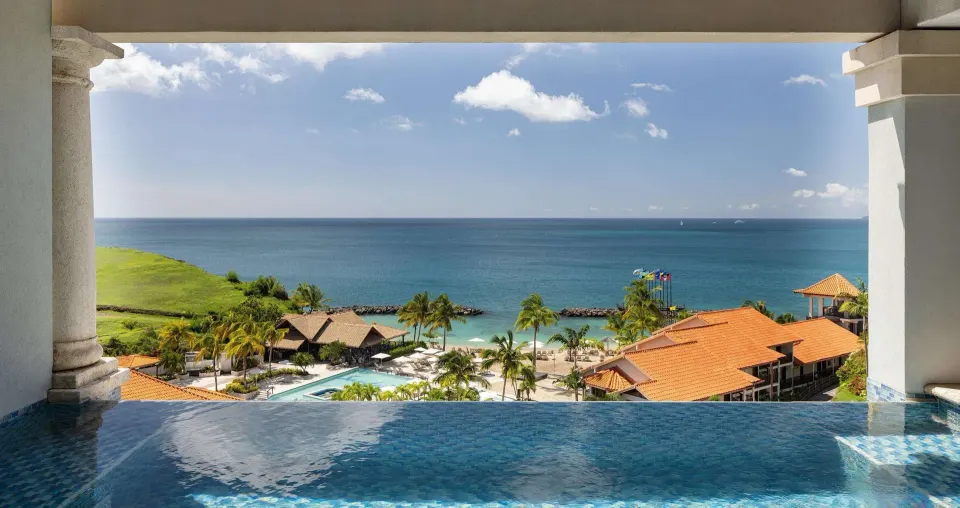 Infinity pool edge overlooking the beach, ocean, and resort rooftops at Sandals Grenada.