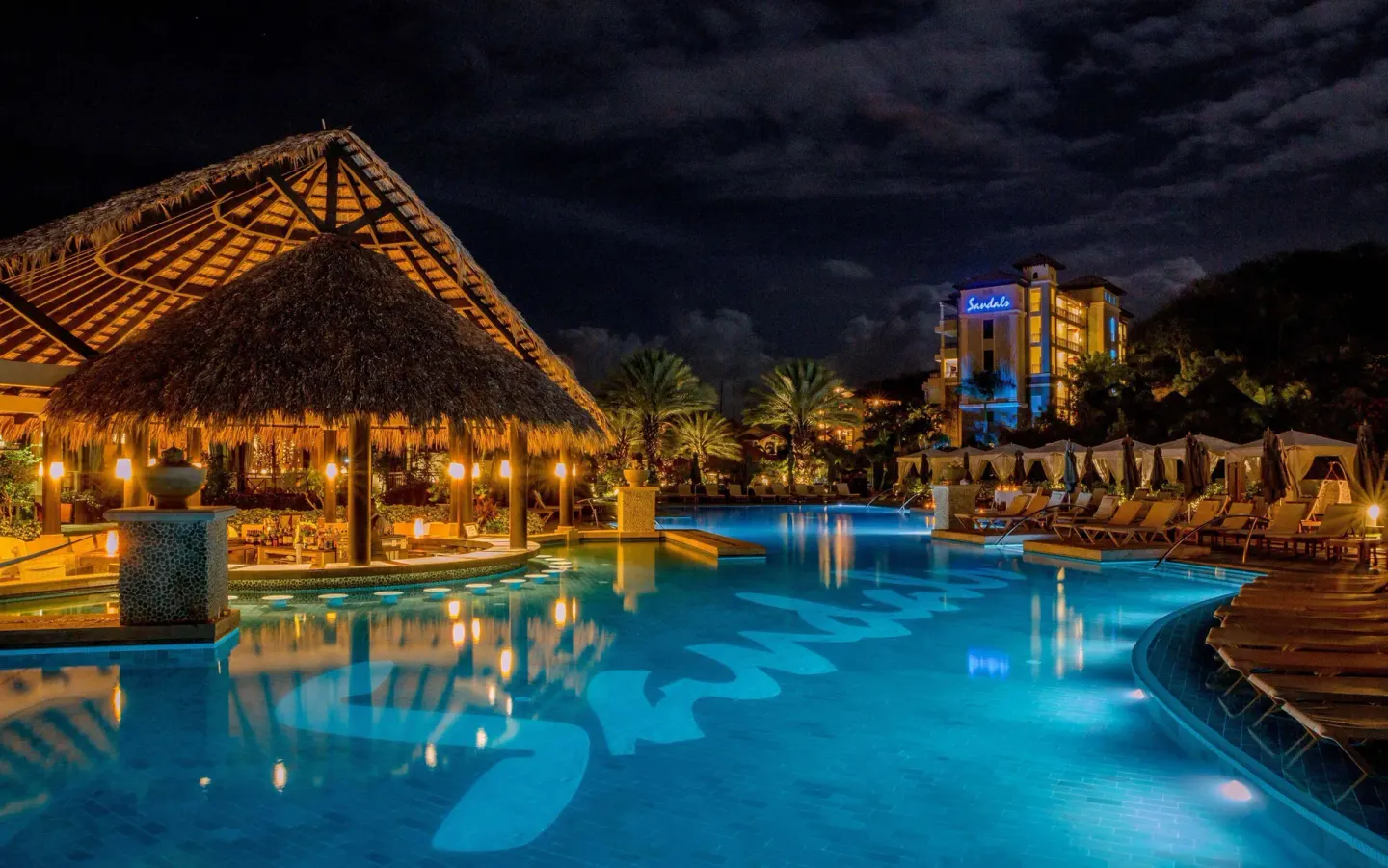 Illuminated resort pool and thatched pavilion at night at Sandals Grenada.