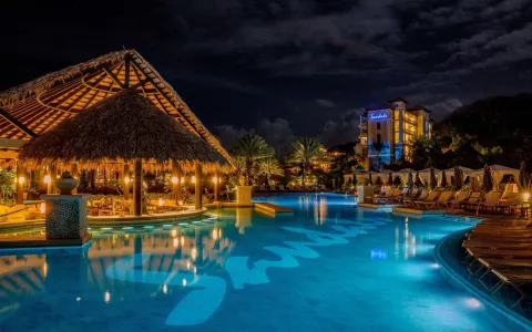 Illuminated resort pool and thatched pavilion at night at Sandals Grenada.