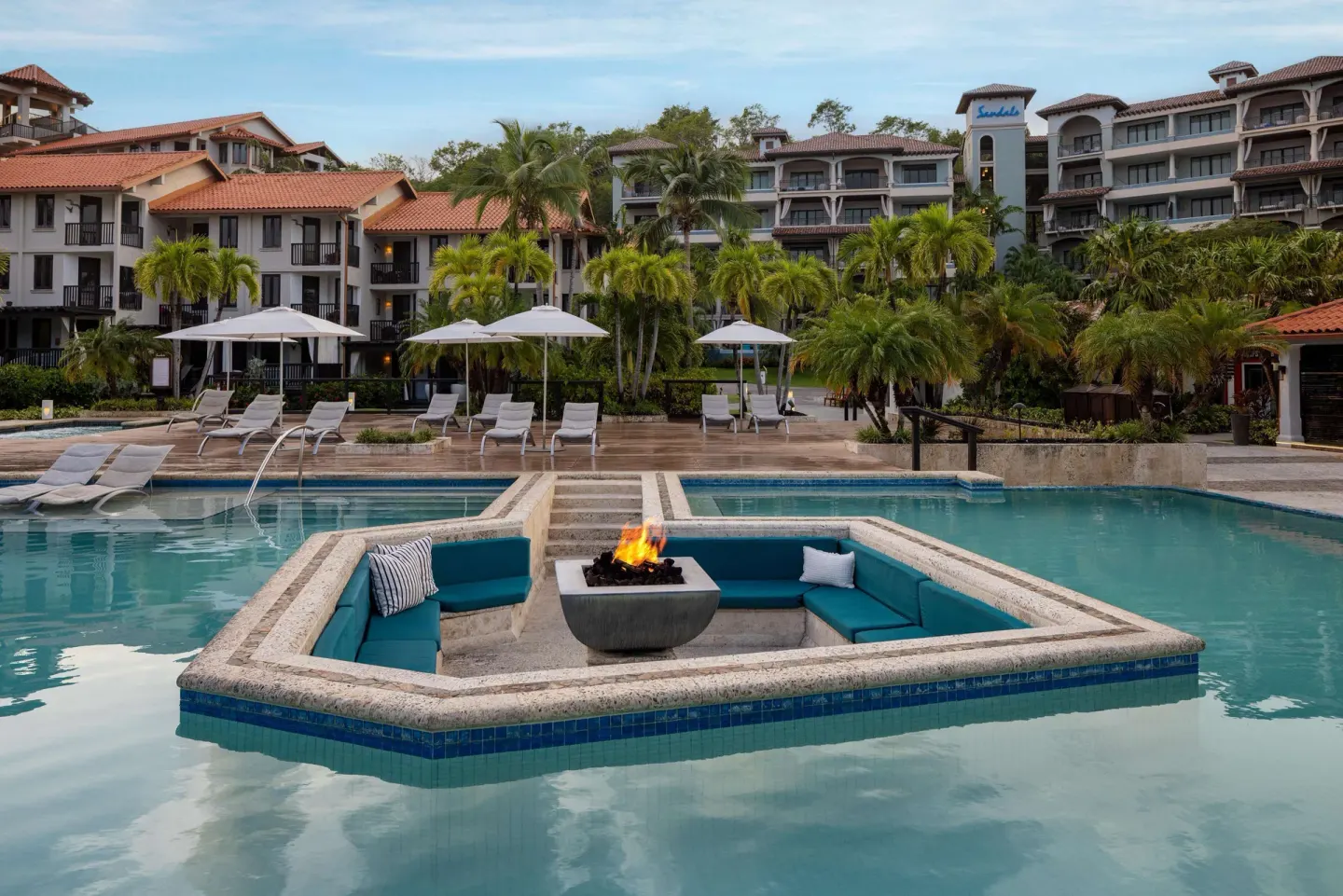 Pool with sunken fire pit seating and resort buildings at Sandals Grenada.