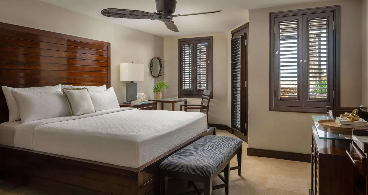 King bed with wood headboard and shuttered windows in a guest room at Sandals Grenada.