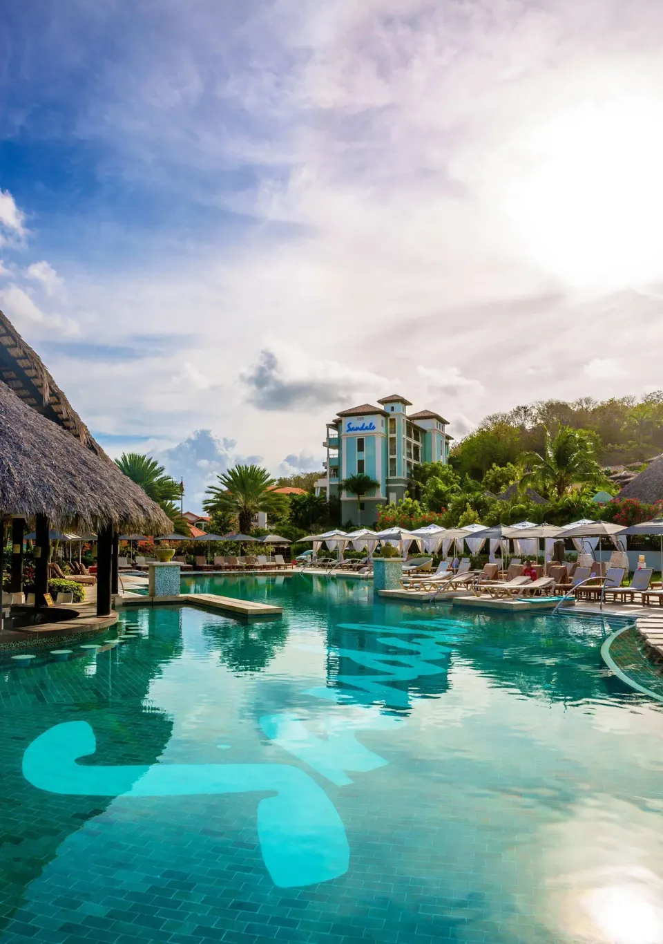 Sunny resort pool with loungers, umbrellas, and a tower building at Sandals Grenada.