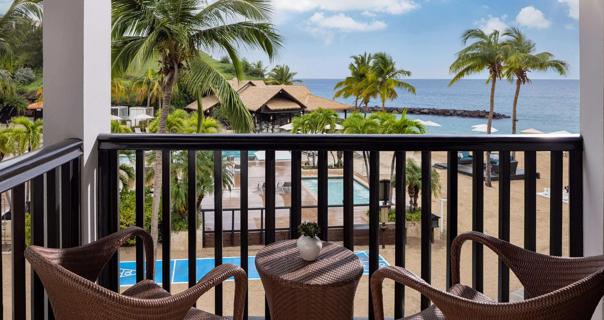 Balcony seating with pool, palms and ocean views from a suite at Sandals Grenada.