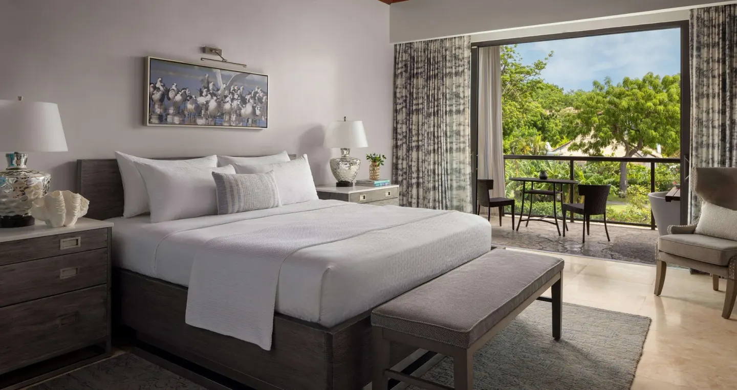 Lover's Hideaway Junior Suite king bed with open garden-view balcony at Sandals Grenada.