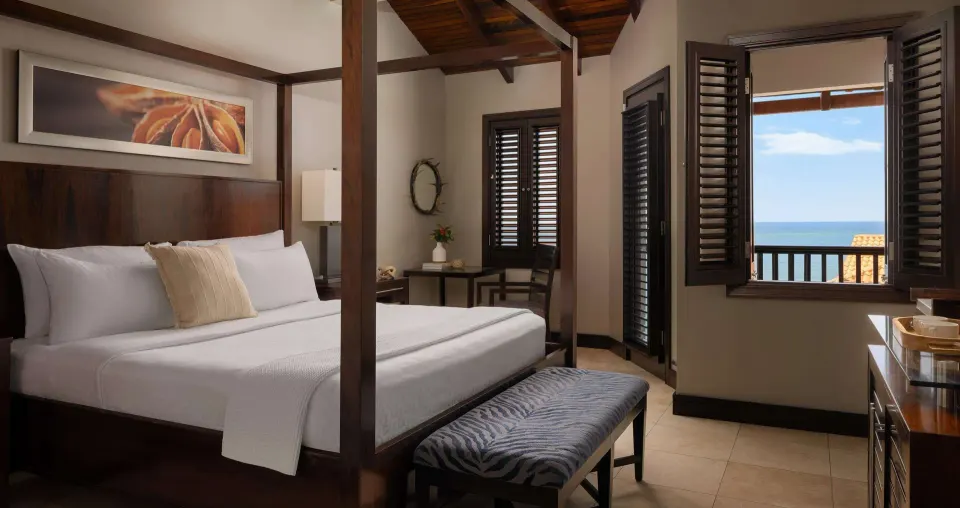Four-poster king bed and ocean-facing window in a room at Sandals Grenada.