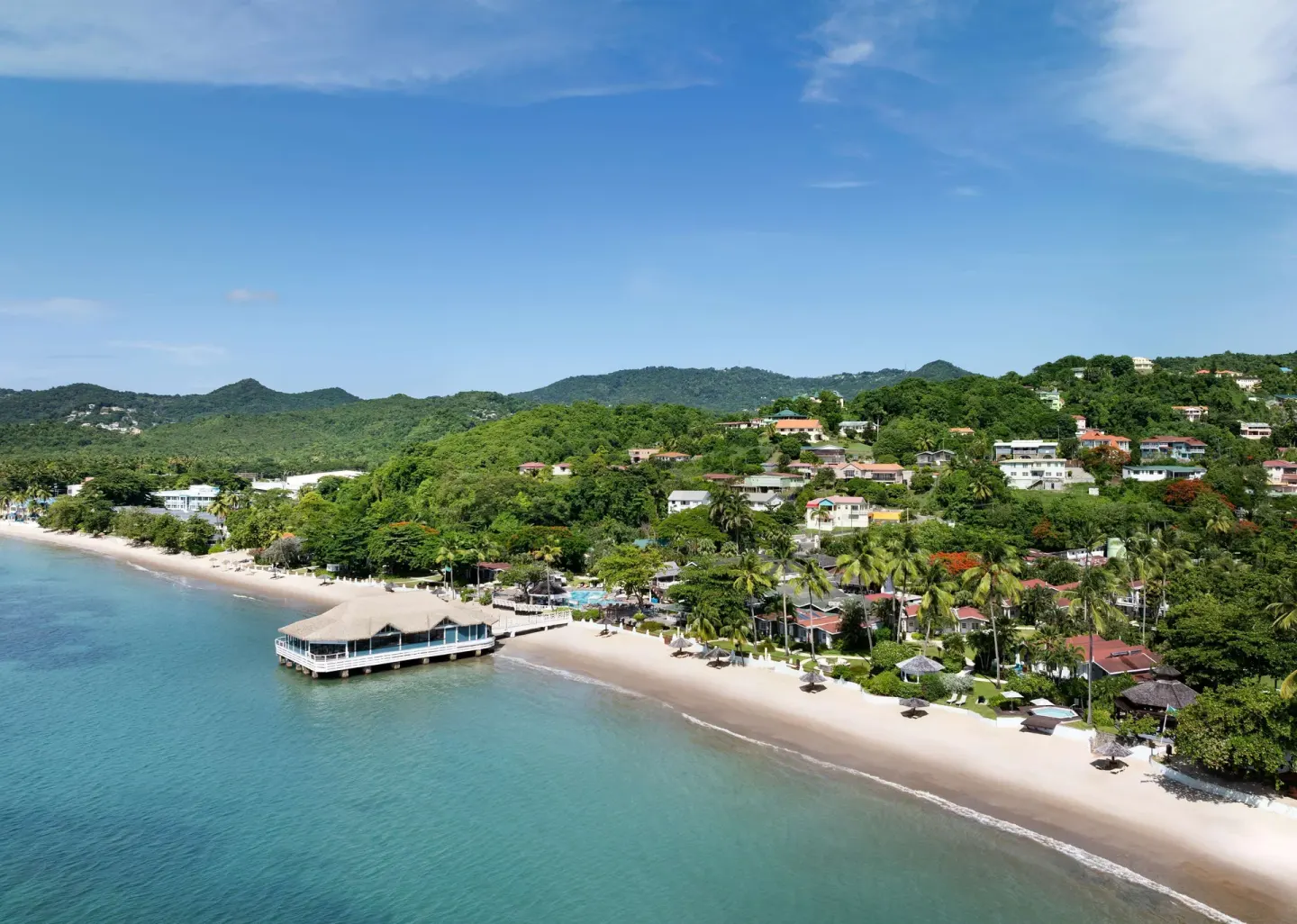Aerial coastline view with beach, palms, and overwater pier at Sandals Halcyon.