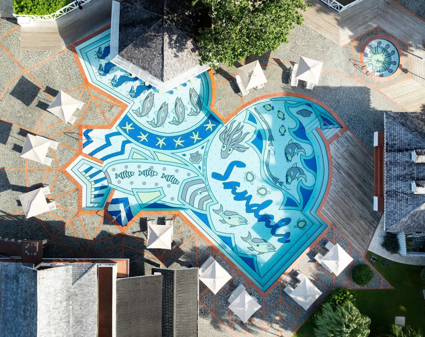 Aerial view of a fish-shaped plaza mosaic with umbrellas and rooftops at Sandals Halcyon.