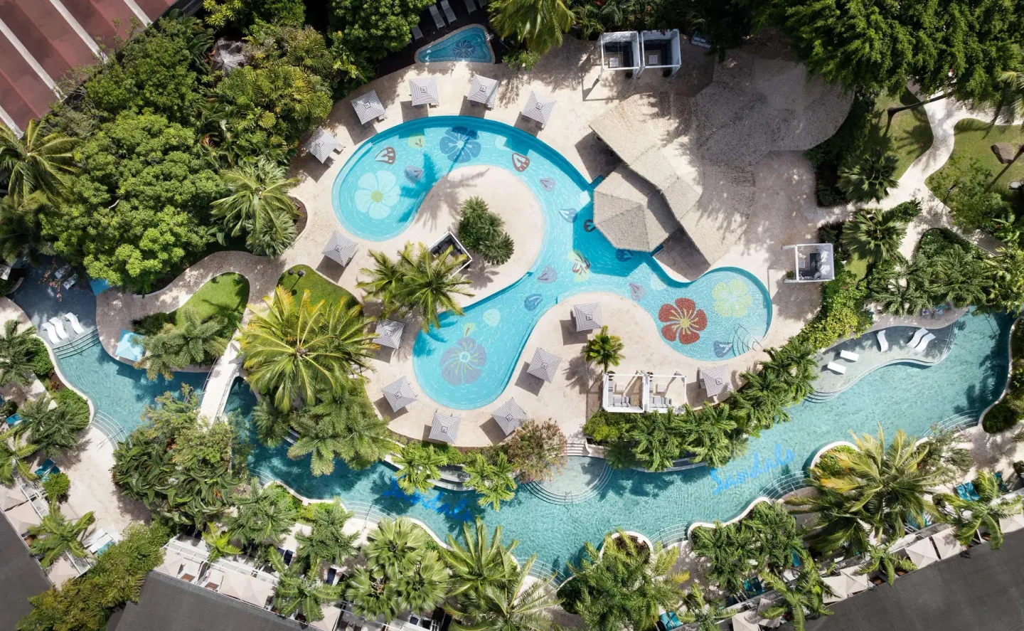 Aerial view of connected pools, palm trees, loungers, and cabanas at Sandals Halcyon.